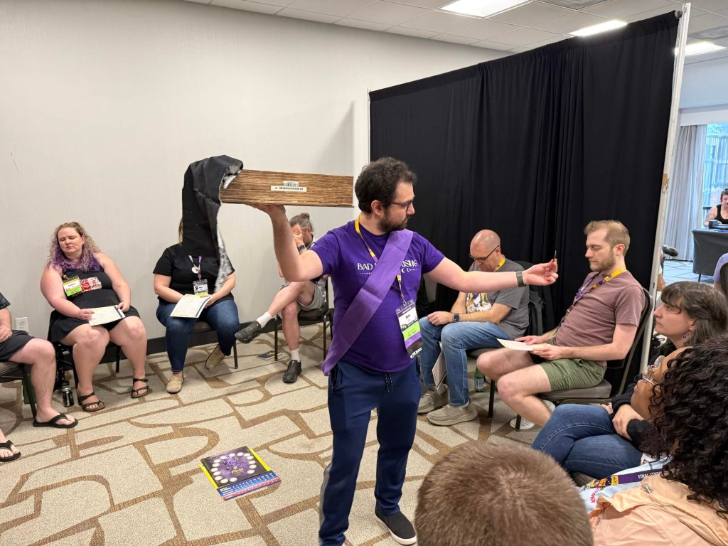 Ekin holding a grimoire, Storytelling a game. He's showing a night card to a player.